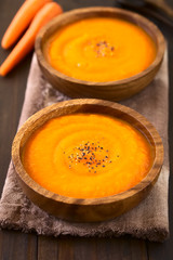 Fresh homemade cream of carrot soup with freshly ground black pepper, photographed on dark wood with natural light (Selective Focus, Focus in the middle of the first soup)