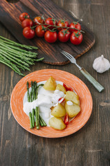 Potatoes and asparagus with tomatoes and tartar sauce on plate ready to eat.