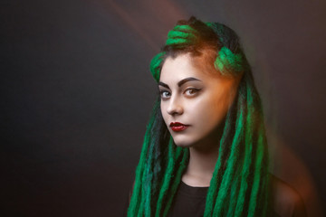 Pretty girl with green long dreadlocks. Black background. Mixed light.