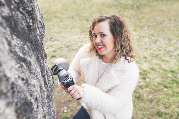 Beautiful curly woman wearing fur coat and posing an angle grinder at park. International Woman's...