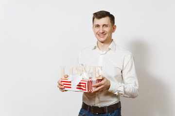 Young smiling man holding wooden word Love, red present box with gift isolated on white background. Copy space advertisement. St. Valentine's Day, International Women's Day, birthday, holiday concept.