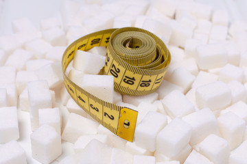 Diet without sugar to reduce weight. A pile of white sugar cubes and a yellow measuring tape on it.