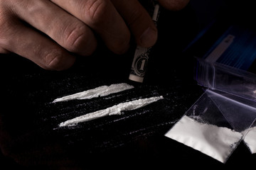 Drug addiction. Junkie man sniffs a line of cocaine through a dollar, sachets with a dose. Black...