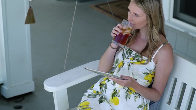 Young woman with drink using digital tablet on porch