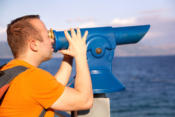 Man tourist and traveler using, watches and looks natural environment in telescope telescope at beach of Adriatic Sea, Mediterranean / Panorama and view of sea and sky.