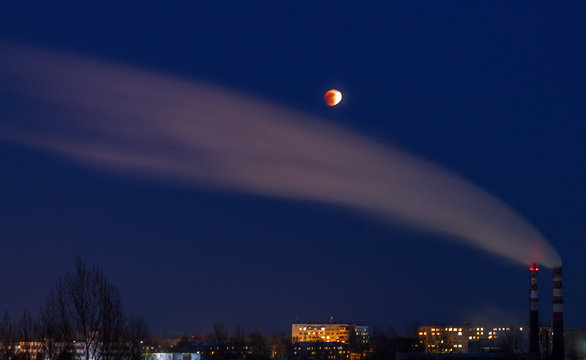 Lunar eclipse on January 31, 2018 against the background of a dark sky and smoke from a pipe. Eclipse, the super moon, the full moon. Western Siberia. The peak phase of the lunar eclipse.