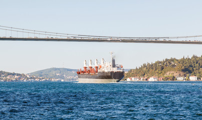 Fototapeta premium Large cargo ship proceeding along the Bosphorus Channel on the background of the bridge on the background
