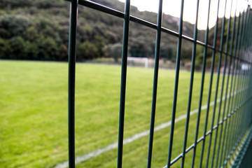 Detail of a soccer field with white line and fence / Close up metallic net-shaped green fence on a background of football field.