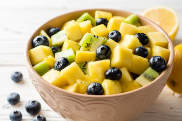 Fresh fruit salad with pineapple, mango, kiwi and blueberries on white wooden background.