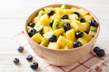 Fresh fruit salad with pineapple, mango, kiwi and blueberries on white wooden background.