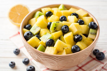 Fresh fruit salad with pineapple, mango, kiwi and blueberries on white wooden background.