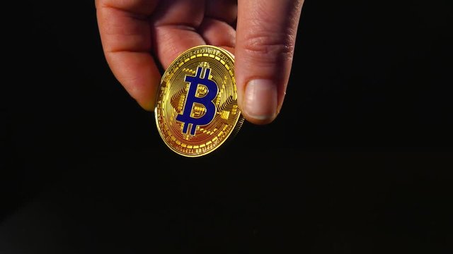 A woman's hand holds a gold coin of bitcoin. Isolated black background.