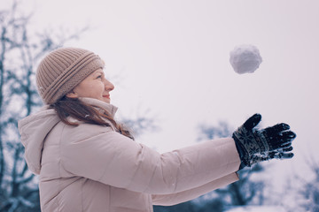 Blonde girl in light clothes throws a snowball