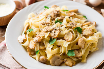 Tagliatelle pasta with mushrooms, parsley and Parmesan cheese on wooden table.