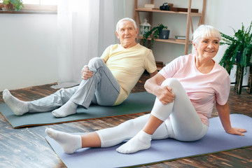 Senior couple doing yoga together at home health care leg stretching - Powered by Adobe