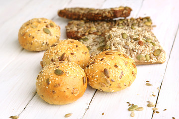 Bread buns with various seeds on white wooden table. Bread roll and breadsticks with sesame, pumpkin, sunflower, flax seeds, 
