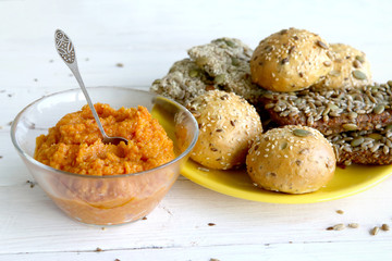 Pumpkin dip in glass bowl  and bread buns with various seeds and on white wooden table. Bread roll and breadsticks with sesame, pumpkin, sunflower, flax seeds and vegetable sauce. 