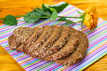 The food is a composition of fresh chopped bread and one yellow rose, which are on a napkin on a yellow wooden background.