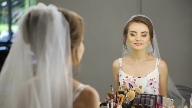 beautiful young woman in white nightgown looks at herself in the mirror