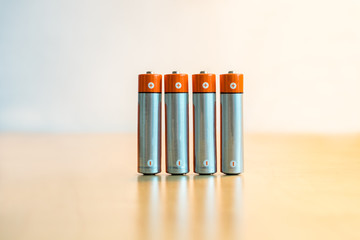 Close-up of four AA batteries standing on a table with plus and minus signs.