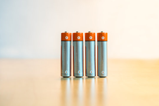 Close-up of four AA batteries standing on a table with plus and minus signs.