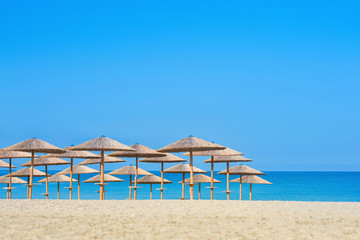 View of tropical beach with big straw umbrellas and sun loungers on the sunset sea background