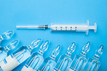 Top view of medical ampoules and syringes on blue background.