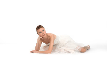 The ballerina in a dress rests on a floor and smiles.