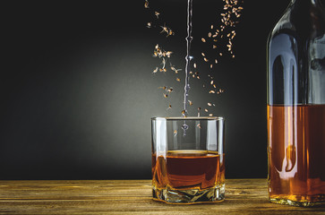 A glass and a bottle of whiskey on a wooden surface. In the glass drops the ingredients from which the drink is created.
- 190434860