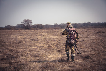 Chasseur en tenue de camouflage avec fusil de chasse traversant un champ rural pendant la chasse