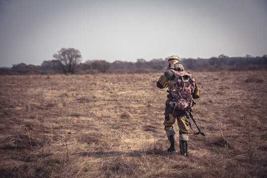 Hunter man in camouflage with shotgun going through rural field during hunting