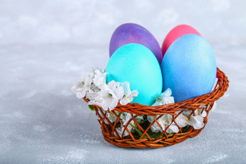 Colored Easter eggs in a basket on a gray concrete background.
