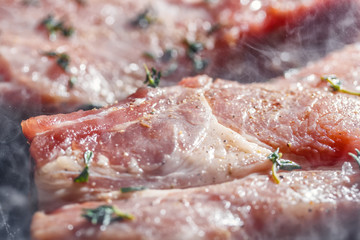 Smoke rises above natural pork cutlets with seasoned pepper, salt, garlic and thyme, frying in a grill pan