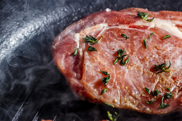 Smoke rises above natural pork cutlets with seasoned pepper, salt, garlic and thyme, frying in a grill pan