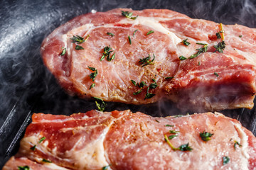 Smoke rises above natural pork cutlets with seasoned pepper, salt, garlic and thyme, frying in a grill pan