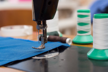 The old sewing machine is sewn blue cloth in the home workshop