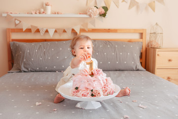 Fototapeta na wymiar Portrait of cute adorable Caucasian blonde baby girl in white dress celebrating her first birthday. Home indoors cake smash first year concept