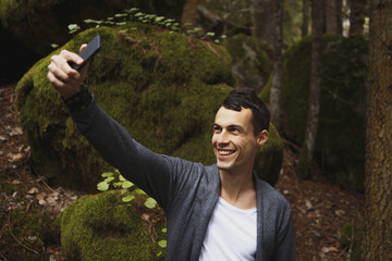 Man takes a picture on mobile phone in the pine forest on a cold sammer day