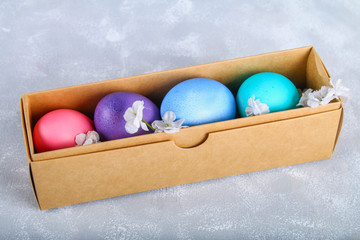 Colored Easter eggs in a gift box on a gray concrete background.