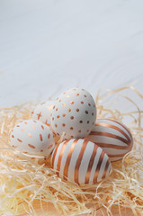 Golden Easter eggs in straw nest on white wooden rustic vintage background.