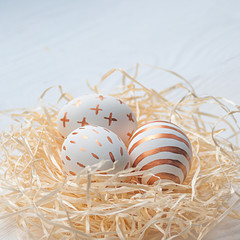 Golden Easter eggs in straw nest on white wooden rustic vintage background.