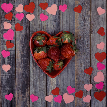 Heart shaped bowl of strawberries on wooden background