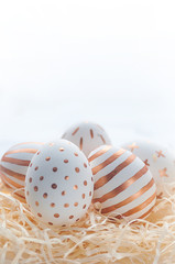 Golden Easter eggs in straw nest on white wooden rustic vintage background.
