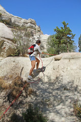 The young woman rises by the steep hill by means of rope. Rock formation at the end of the Zemi valley between Gereme and Uchisar, Cappadocia, Turkey.