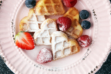 Traditional belgian waffles with fresh fruit and powder sugar on wooden board