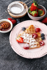 Traditional belgian waffles with fresh fruit and powder sugar on wooden board
