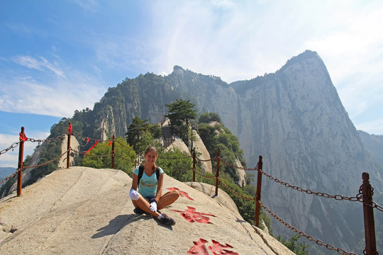 A free young girl hiker is sitting at mountain peak, Huashan Mountain, Xian, China.