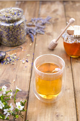 A fragrant herbal tea with lavender. In a glass with double walls. A bank of dried herbs for tea. Branch with flowers. Bank with honey. Free space for text or a postcard.