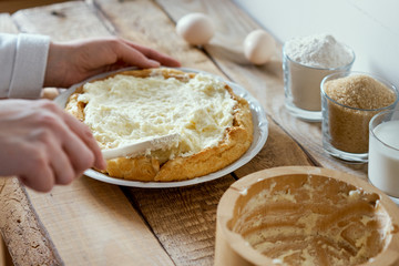 woman puts a cream on the cake on an old wooden table