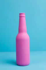 Close up of pink beer bottle on blue background. Deceptive attraction of alcohol.  Alcoholism addiction, alcohol abuse and alcohol dependence concept.